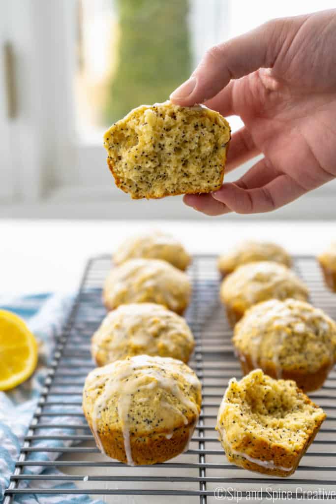 Hand holding a lemon poppy seed muffin over a tray of muffins