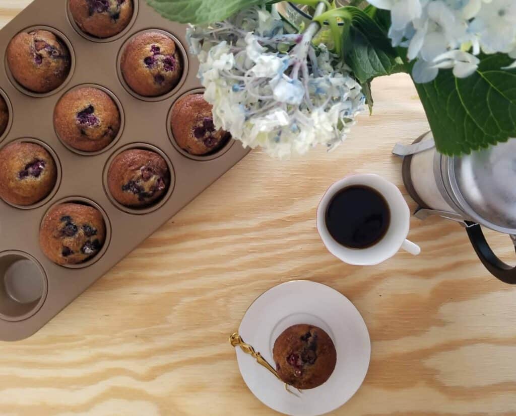 Overhead of blueberry muffins and cup of coffee on wooden board