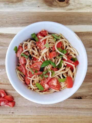 fresh summer tomato pasta with basil in a white bowl on a wooden board