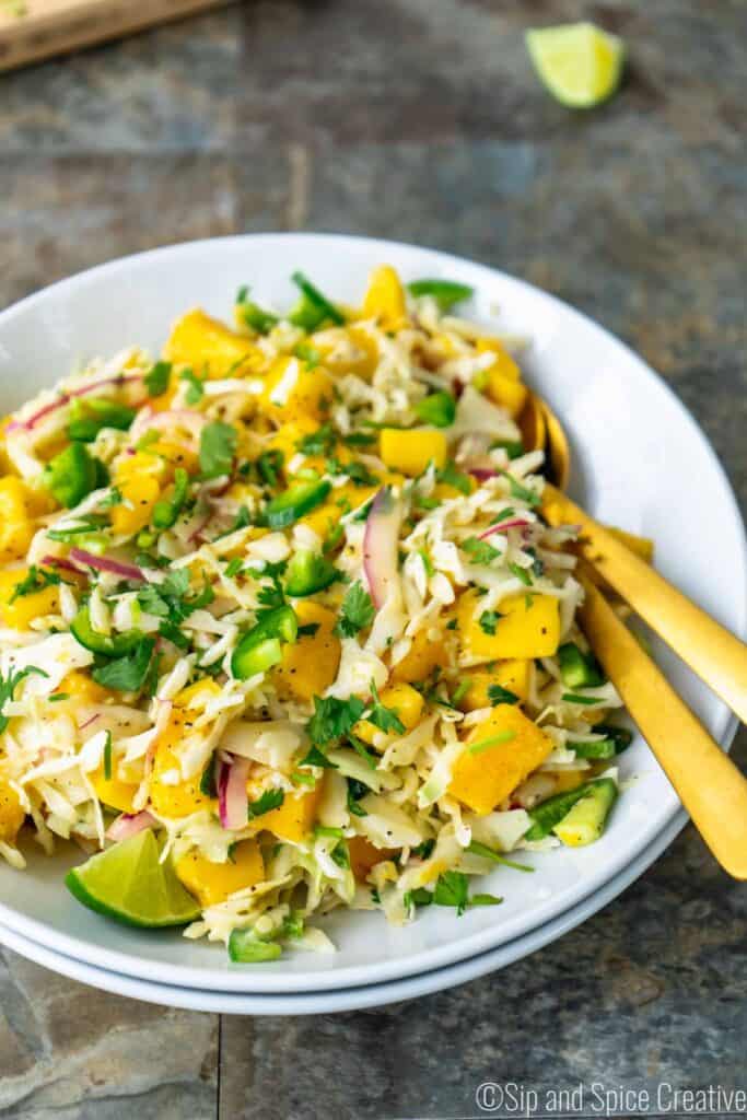 Spicy Mango Slaw in a white bowl with gold silverware
