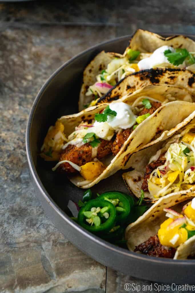 blackened fish tacos with crema and mango slaw in a grey bowl