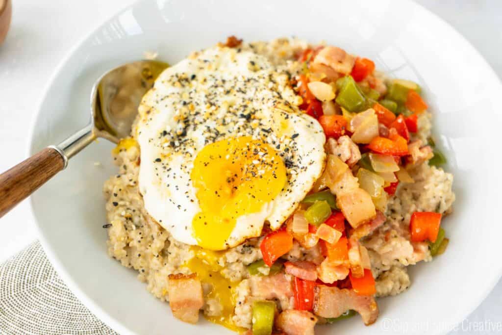 savory oatmeal topped with bacon, peppers and onions and a fried egg with the yolk broken