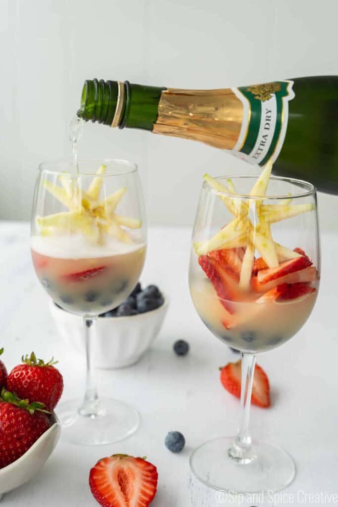 champagne pouring into wine glass over red white and blue fruit