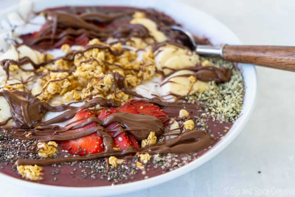 nutella acai bowl with strawberries, chia seeds, hemp seeds with wooden spoon