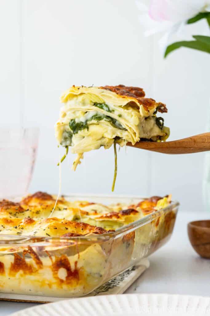 slice of spinach artichoke lasagna being lifted from the pan