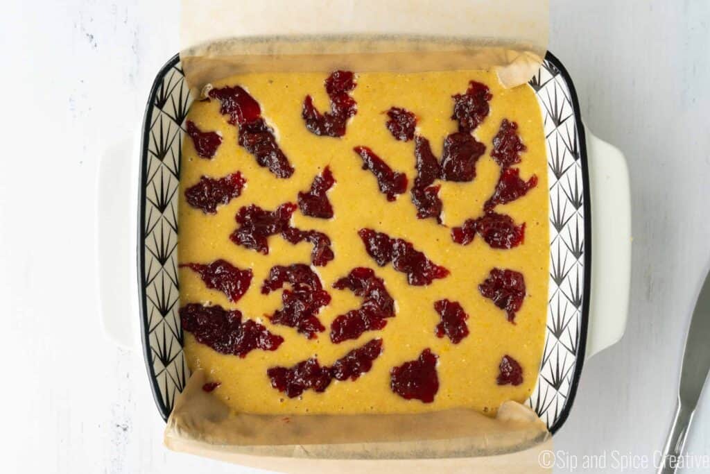raw cake batter in square pan with strawberry jam dropped throughout