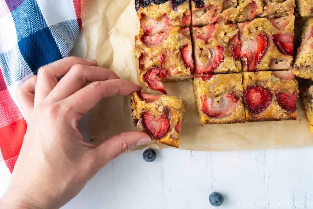 hand grabbing corner slice of cake topped with strawberries 