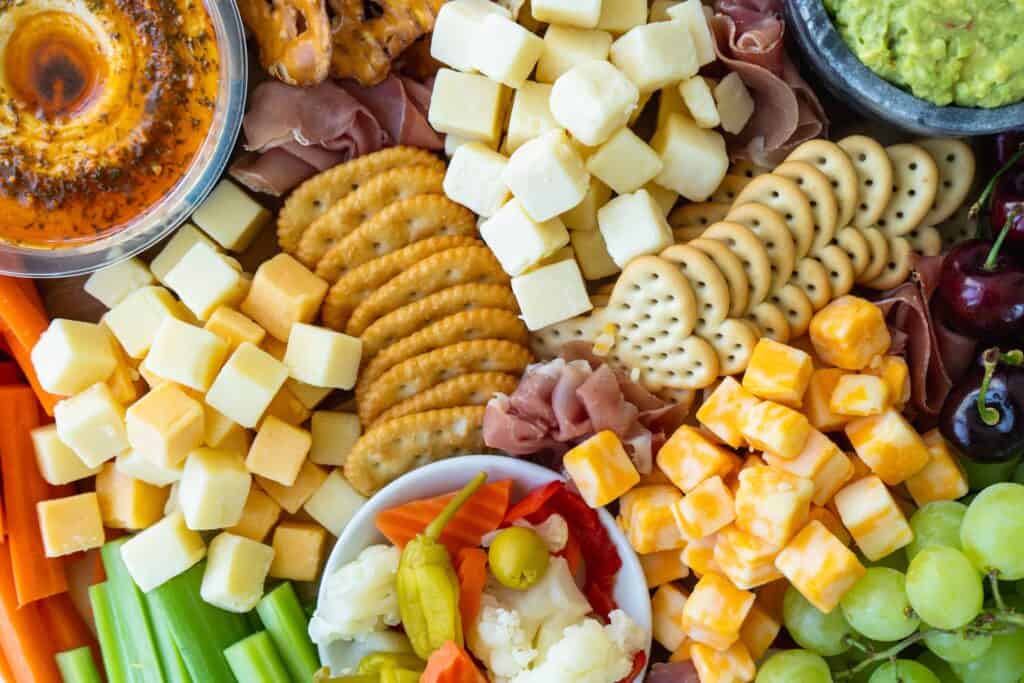 closeup of cheeseboard with crackers, cheesecubes, hummus, prosciutto