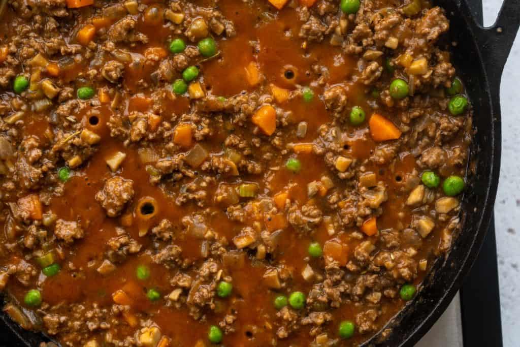 shephard's pie filling of ground beef, carrot and peas bubbling in the cast iron skillet