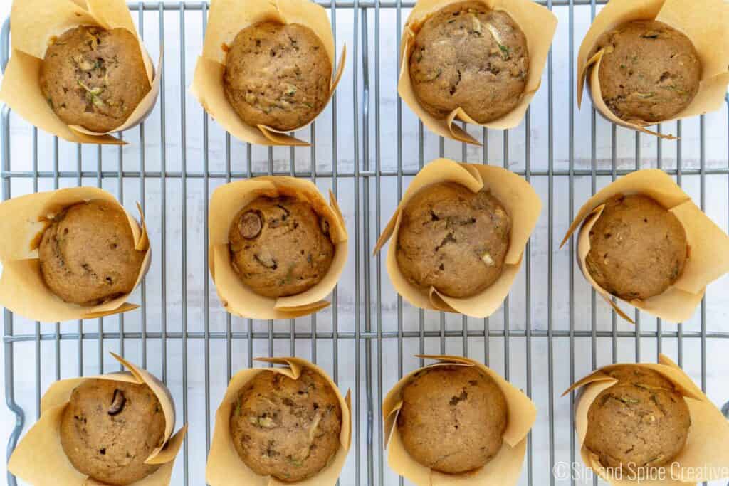 zucchini muffins, some with chocolate chips in paper wraps on a cooling rack
