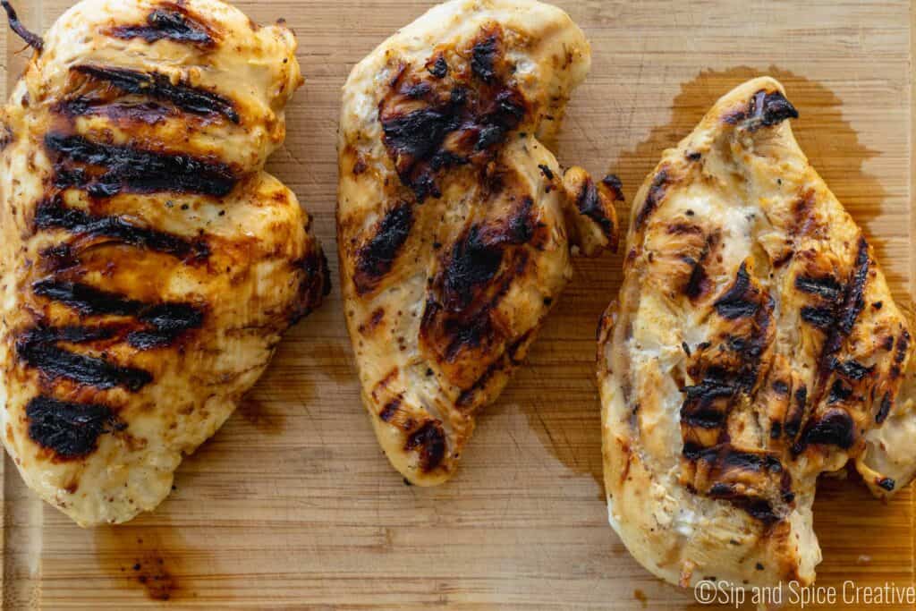 three grilled chicken breasts on a wooden board