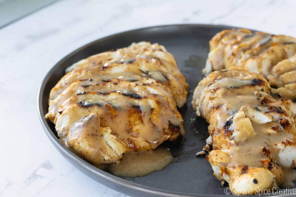 sliced grilled chicken breasts on a grey plate drizzled with honey mustard sauce