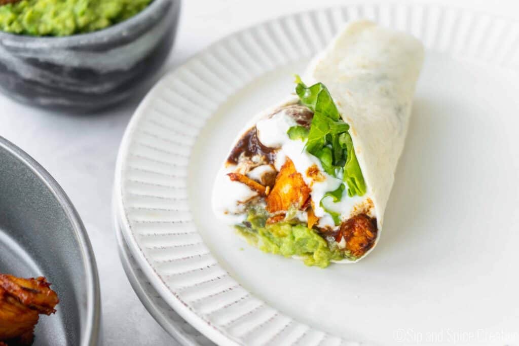 burst tomato and spicy lemon chicken wrap with lettuce, guacamole and greek yogurt on a white place