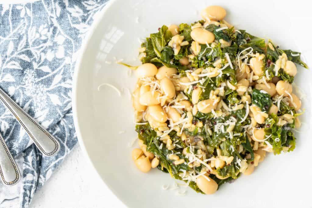 white bowl of greens and beans risotto with a blue napkin
