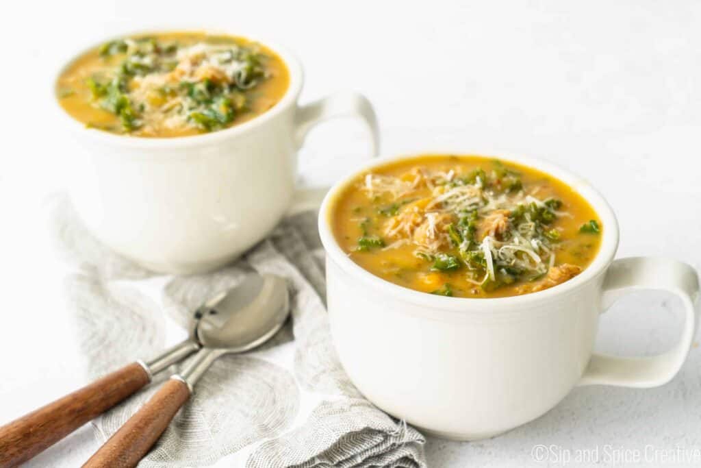 two white mugs of Creamy Sweet Potato Kale Soup with Sausage  with wooden soons