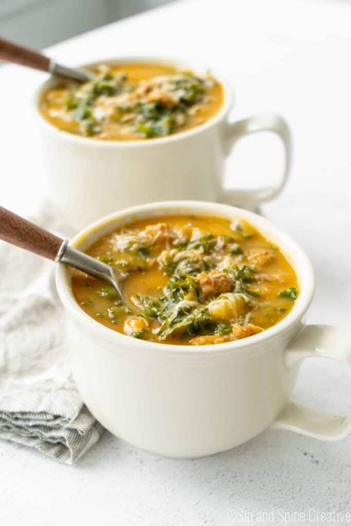 two mugs of creamy sweet potato kale soup with sausage with two wooden soups