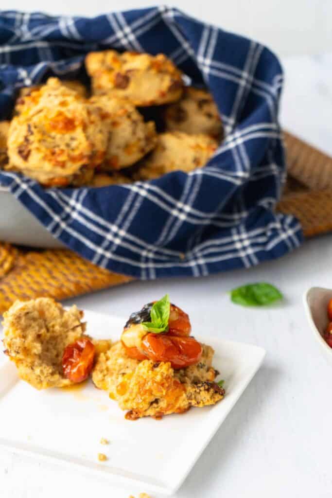 Cheesy Meatball-Studded Drop Biscuits in a basket with one on a plate topped with roasted tomato