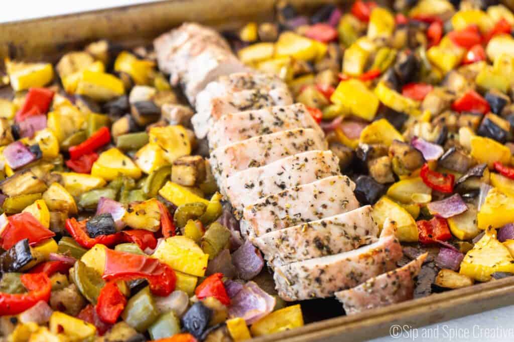 sliced pork tenderloin in the middle of a sheet pan surrounded by roasted vegetables