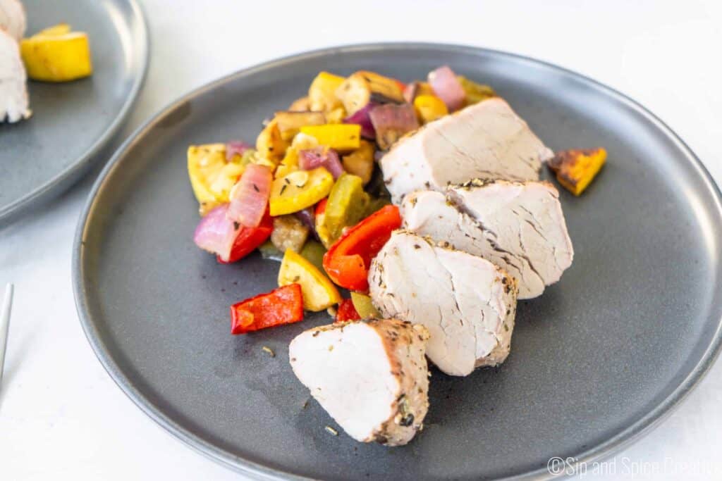 pork tenderloin slices on a grey plate with roasted peppers, onions, eggplant