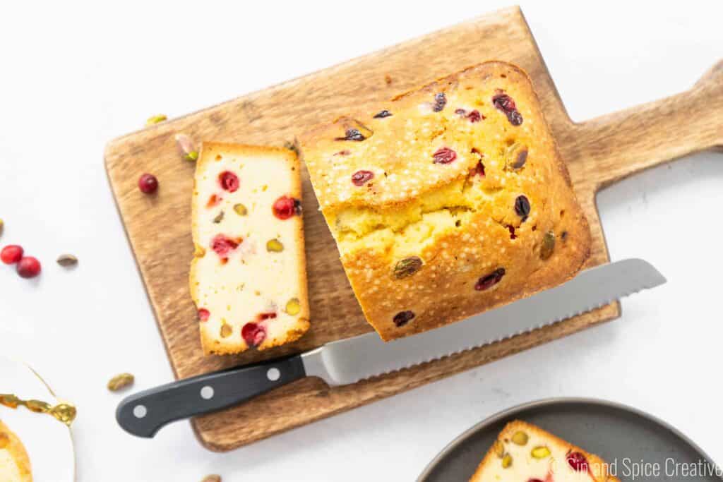 cranberry pistachio pound cake on a wooden cutting board with a bread knife