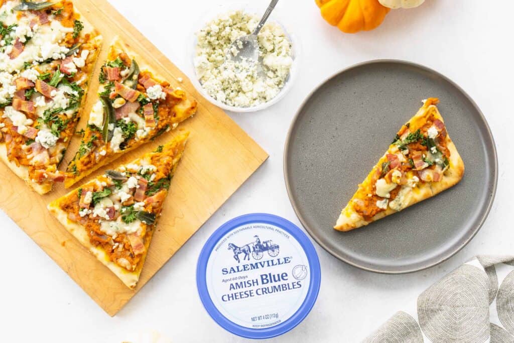 Savory Pumpkin Flatbread with Bacon, Sage and Blue Cheese on a wooden board with blue cheese crumbles with slices on flatbread