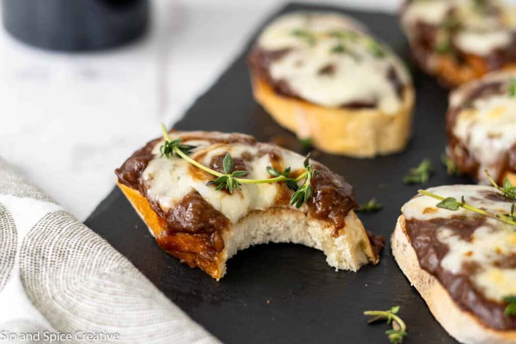 Bite taken out of French Onion Crostini on black slate board