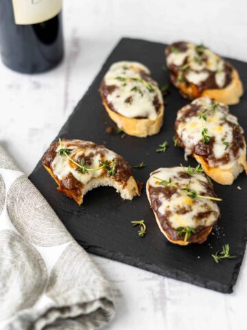 french onion crostini on a black slate plate