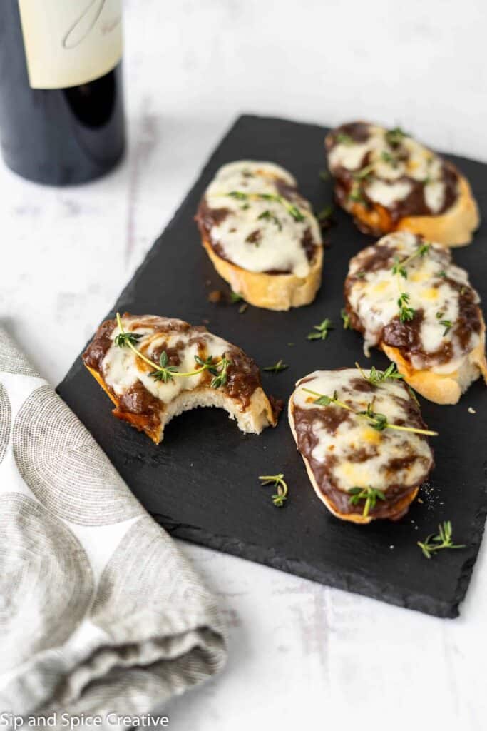crostini on a slate board with thyme springs and a bottle of wine