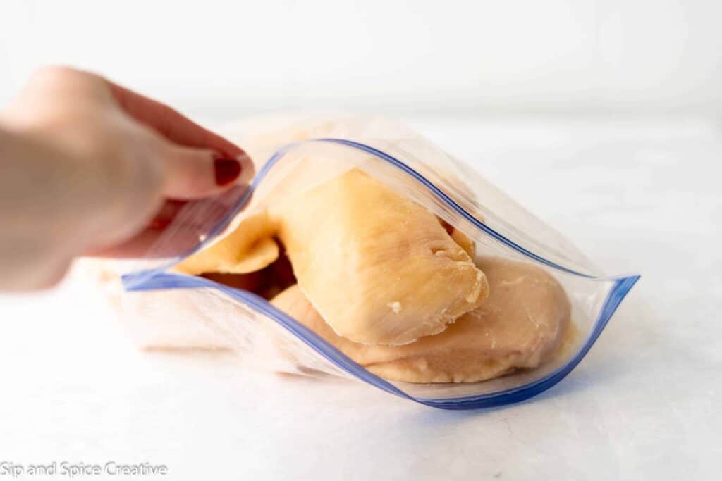 frozen chicken breasts in a ziploc bag held open by a hand