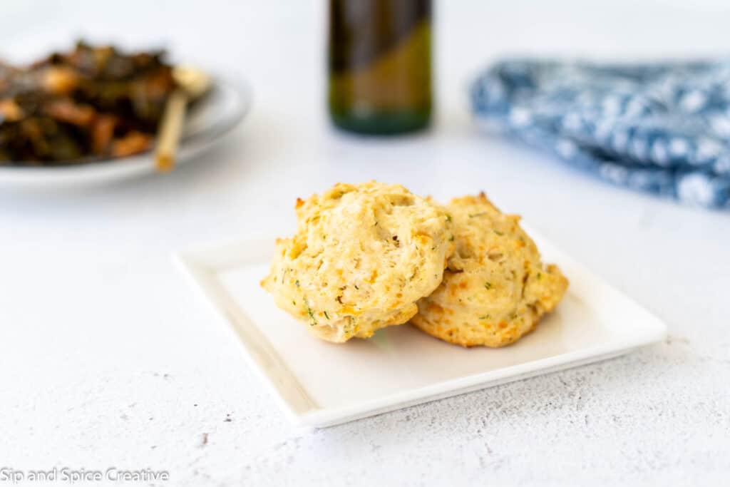 two dill biscuits on a white square plate with a beer in the background