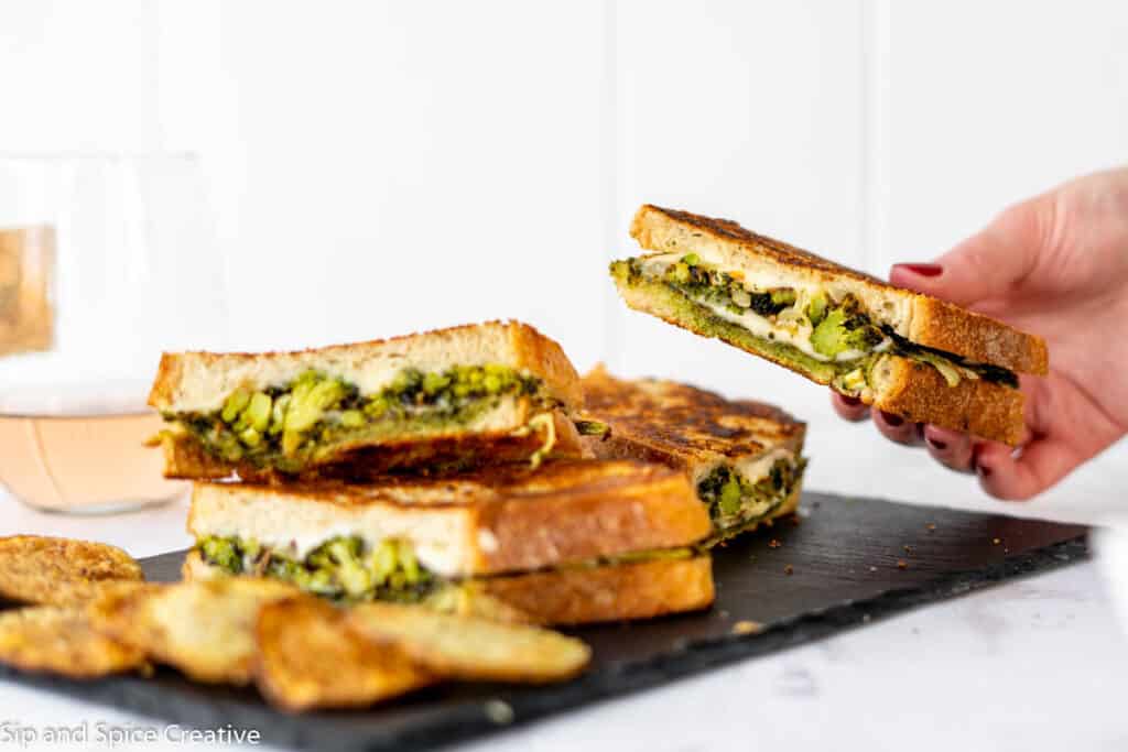 female hand holding a grilled cheese half over a plate of sandwiches with potato chips and rose