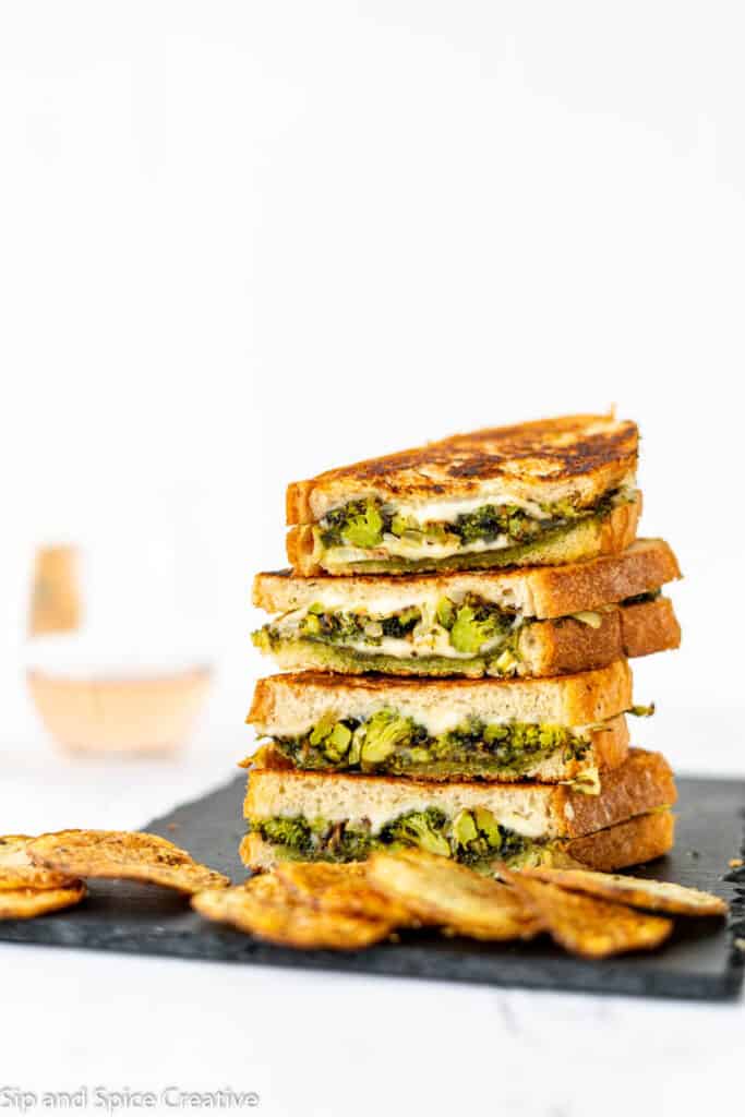 broccoli grilled cheeses sliced in half and stacked on top of each other in a tower with potato chips on a slate board