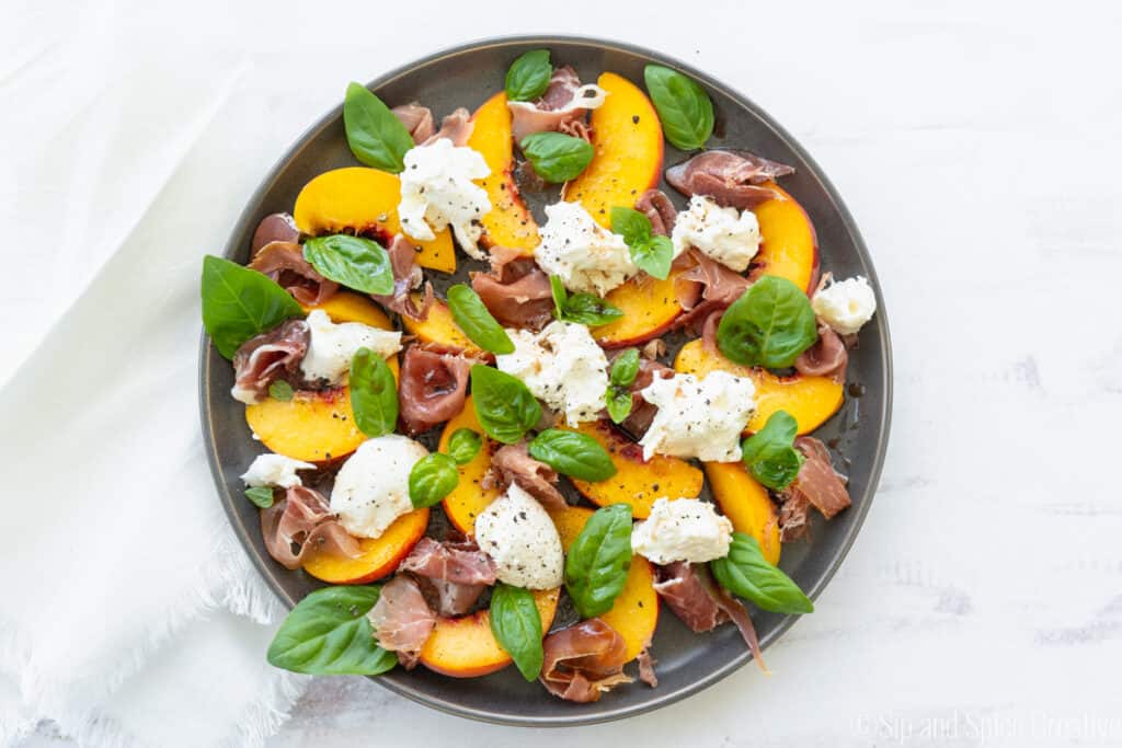 top down view of peach salad with burrata, prosciutto and basil