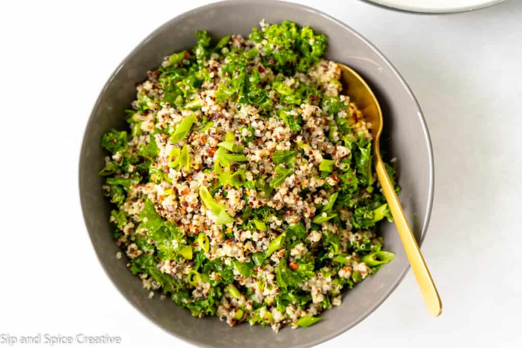 top down view on kale quinoa salad with a gold spoon in a gray bowl on a white background