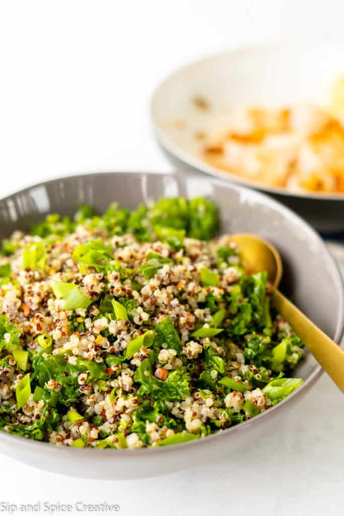 angled view of kale quinoa salad with a gold spoon on the side in a gray bowl