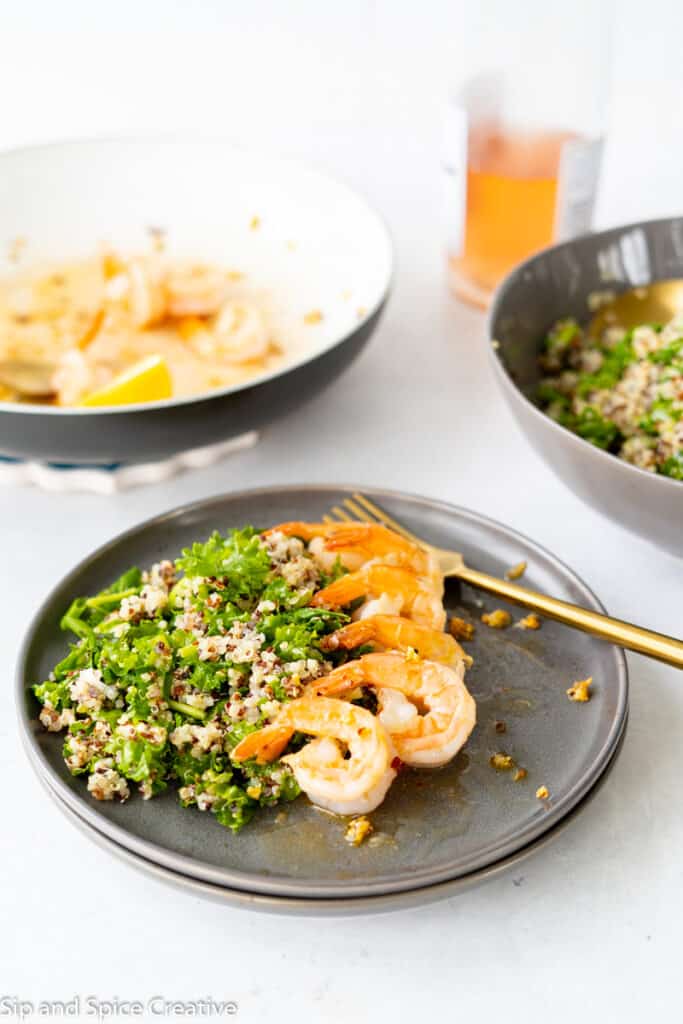 kale quinoa salad on a grey plate with a line of sauteed shrimp with a gold fork