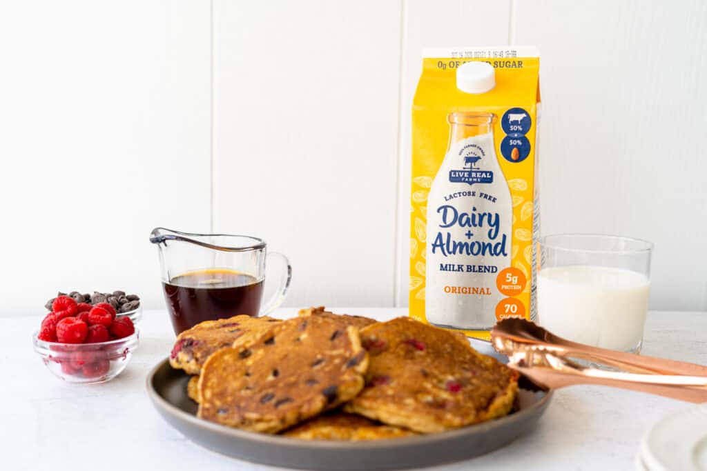 plate of pancakes on a white tabletop with a glass of milk next to milk carton