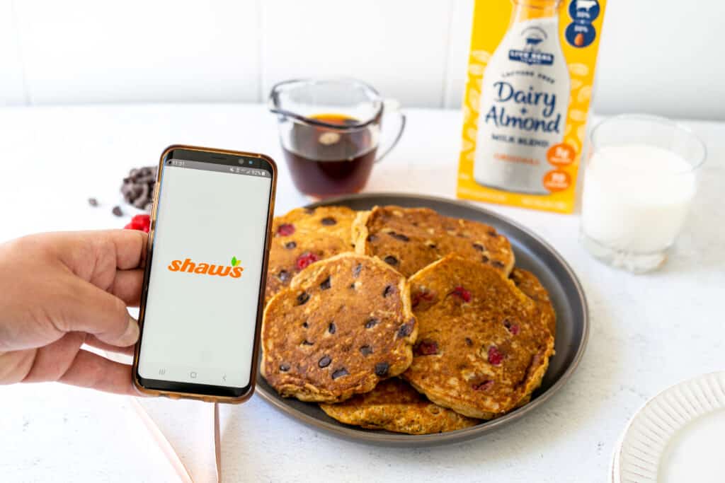 mobile phone with home page of Shaw's app above a plate of pancakes