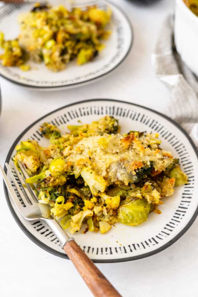 Close up white and blue plate of cheesy winter vegetables gratin with a wooden fork