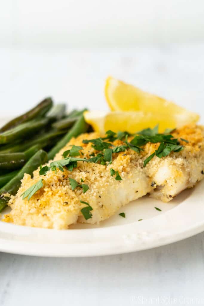 close up shot of flaky white fish with breadcrumbs and lemon slices in the background